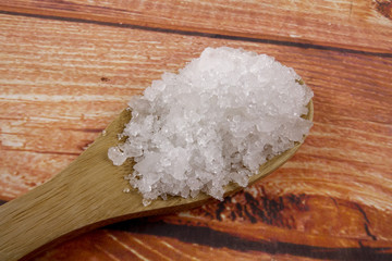 Sea salt in a wooden spoon. Also called bay salt or solar salt, is used in cooking and cosmetics. Rough grained crystals of the mineral.