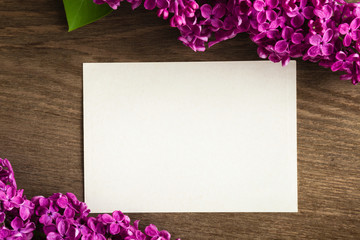 Purple lilac flowers with blank greeting card on the wooden table.