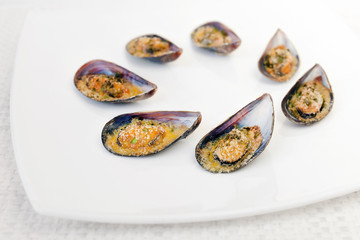 Gratin mussels. Grilled mussels cooked in the oven, accompanied by slices of lemon, grated pan and parsley. Mussels cooked on white plate.