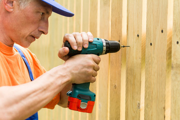 Portrait of a handyman,  concentrating at work with a screwdriver when constructing a wooden fence