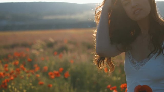 Young woman with long brunette hair walking among blooming poppy flowers