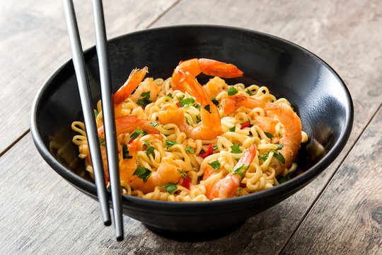 Noodles and shrimps with vegetables in black bowl on wooden table
