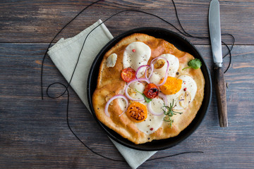 Small homemade pizza with mozzarella cheese, tomatoes, herbs on rustic wooden table. Top view.