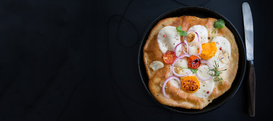 Small homemade pizza with mozzarella cheese, tomatoes, herbs on rustic wooden table. Top view. Copy space. Wide panoramic image. Copy space.