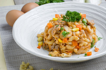 Fried macaroni with egg and pork and vegetable in tomato sauce in plate on a wooden table.