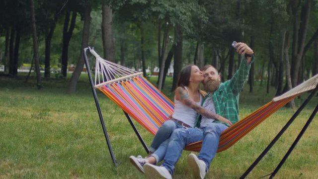 Young couple with mobile phone sitting on hammock. Fall from the hammock to the grass