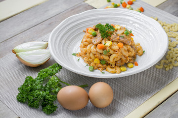 Fried macaroni with egg and pork and vegetable in tomato sauce in plate on a wooden table.