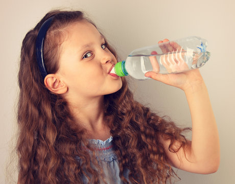 Beautiful long curly hair style smiling kid girl drinking water from the bottle. Toned vintage portrait