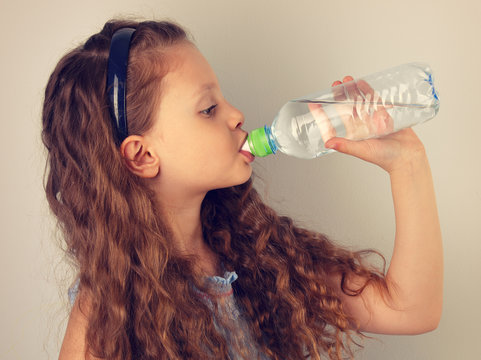 Profile of beautiful long curly hair style smiling kid girl drinking water from the bottle. Toned vintage portrait