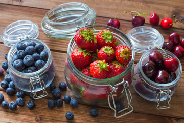 Fresh seasonal fruits in jars / blueberries, strawberries and cherries on a wooden table.