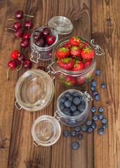 Fresh seasonal fruits in jars / blueberries, strawberries and cherries on a wooden table.