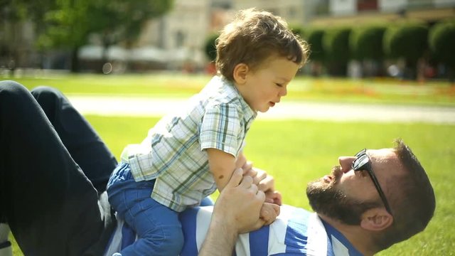 Man cuddling and kissing his son while lying together on the grass
