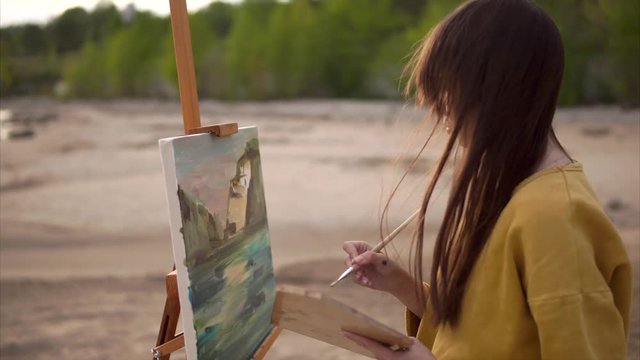 Young woman painter drawing oil landscape painting on easel. Bank of the river. Creative person