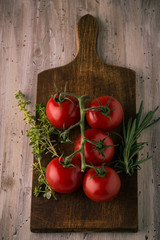 Few red cherry tomatoes on green branch with herbs