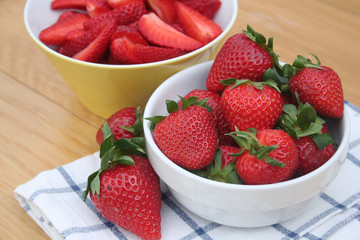 Fragole intere e tagliate su ciotola isolate su tavolo di legno