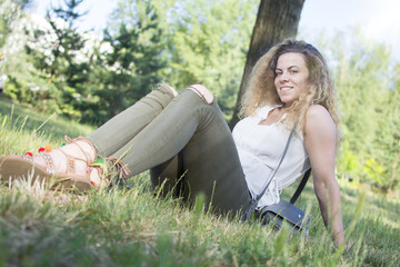 Gorgeous young curly-haired woman relaxing at the city park. Woman in nature, trees in the background.