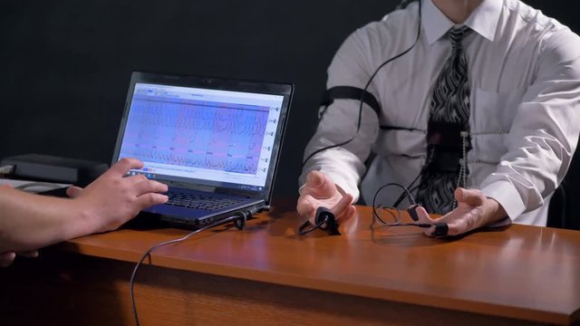 A polygraph computer screen beside operator and subject's hands.