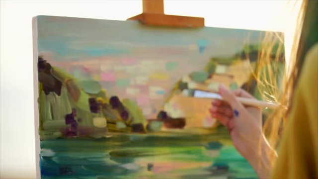 Expressive close up view of girl painter at work. She painting iol picture of abstract landscape. Sunlight in her hair