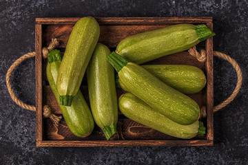 Fresh healthy green zucchini courgettes in brown wooden box.