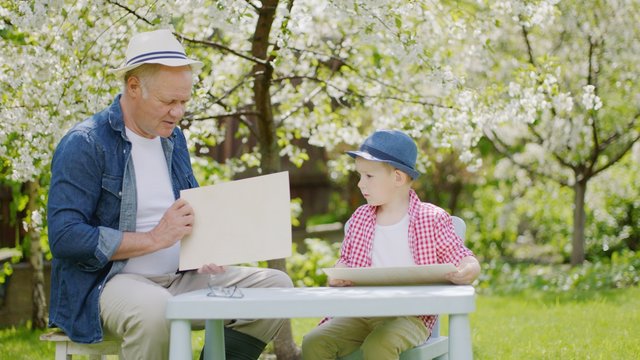 Granddad and his grandson are making wooden plane in the backyard on summertime