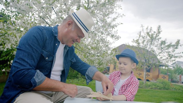 Granddad and his grandson are making wooden plane in the backyard on summertime