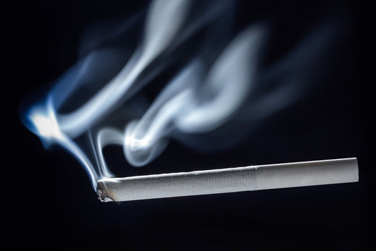 Two unusual white trickles of smoke on a white smoldering cigarette with a filter. Dark background.