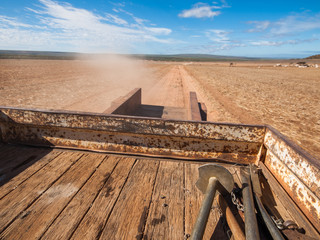 Rusty old Australian cattle truck  driving in a sun drenched arid landscape. A rusty cattle trailer against the vibrant famous orange sand and vibrant blue sky in the western Australian desert.