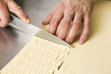 A hand holding a knife cutting a beautiful clean fresh layer of uncooked pastry dough. In preparation for cooking.