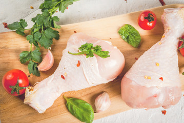 Raw chicken legs. Meat, a source of protein. On a cutting board, on a white stone table. With spices, herbs and tomatoes for cooking. Top view copy space