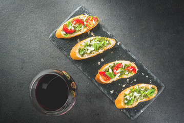 Italian food. Snacks. Antipasto. Bruschetta with pesto sauce, parmesan cheese, tomatoes and fresh basil. On black table, on slate board. With glass of red wine. Top view copy space selective focus