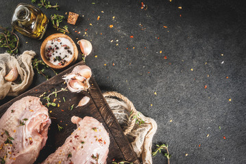 Preparation of food, lunch. Meat. Chicken fillet with skin, raw. On a cutting board, with spices, thyme, garlic, olive oil, salt, pepper. Wooden board, black stone background. Copy space top view
