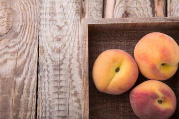 Three peaches in brown wooden box standing on rustic wooden background