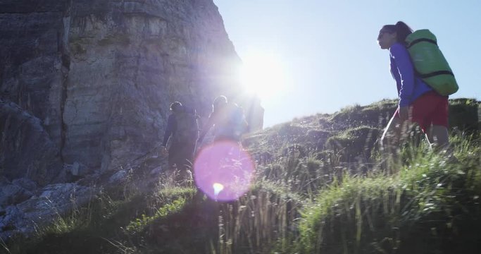 Four friends walking along hiking trail path with sun light flare. Group of friends people summer adventure journey in mountain nature outdoors. Travel exploring Alps. 4k slow motion 60p video