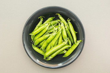 A plate of organic peas in pods on a gray background, the top view.