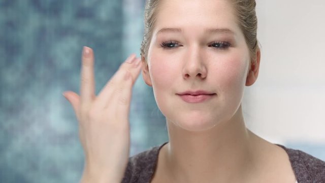 Young caucasian woman applys face cream on her skin