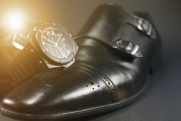 Beautiful black leather men's shoes. Fashionable shoes isolated on black background. Black watch placed on top of shoes.