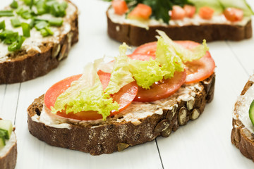 Assortment of vegetarian sandwiches with vegetables and cheese on a white table.