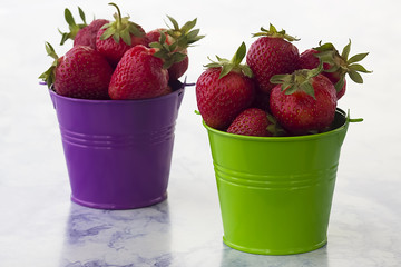 Bright ripe strawberry  in a metal pails  on a light marble background.