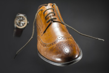 Beautiful brown leather men's shoes. Fashionable shoes isolated on black background. Brown leather watch in the background.