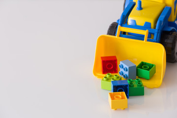 Closeup of children toy tractor with colorful plastic bricks or details on white background. Baby's toys on the table isolated.