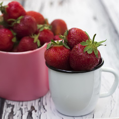 Bright ripe strawberry in a metal mug on a light wooden background.