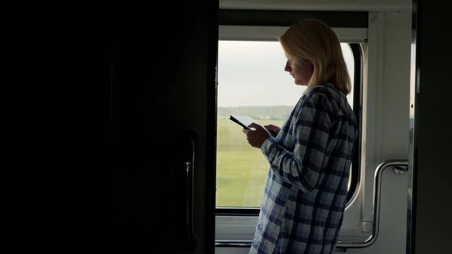 A woman uses a tablet in the train car. Standing by the window, rear view