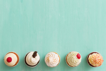 Top view on homemade vanilla, blueberyy, lemon, chocolate cupcakes in row on turquoise retro wooden...