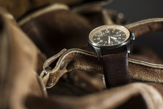 Close up of a beautiful leather watch. Luxury men's watch placed on a leather background. Fashionable brown leather bag with a watch on top of it.