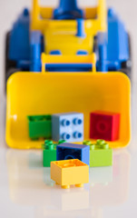 Fototapeta premium Closeup of children toy tractor with colorful plastic bricks or details on white background. Baby's toys on the table isolated.