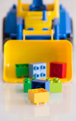 Closeup of children toy tractor with colorful plastic bricks or details on white background. Baby's toys on the table isolated.