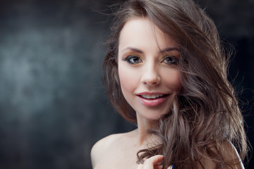 Beautiful brunette girl with luxurious curly hair. Studio portrait on a dark background. Excellent hair