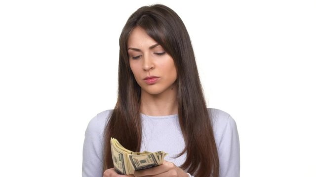 Concentrated beautiful young Caucasian lady counting money holding sheaf of dollars over white background in slowmotion