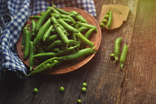 Young peas in a wooden plate on a wooden table. Standing next to a plate of pea pods.