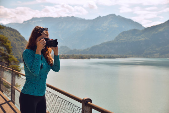 Tourist young girl holding camera and taking photos with beautiful landscape scenery in the back.